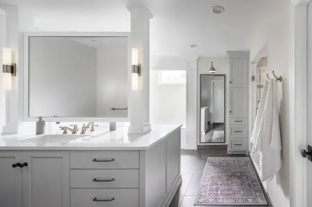 Primary bathroom with gray vanity, white quartz top, brass sconces and a view into the walk-in closet