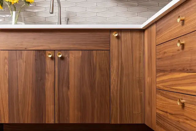 Walnut kitchen cabinets with round brass knobs, white countertop and elongated hexagon tile backsplash