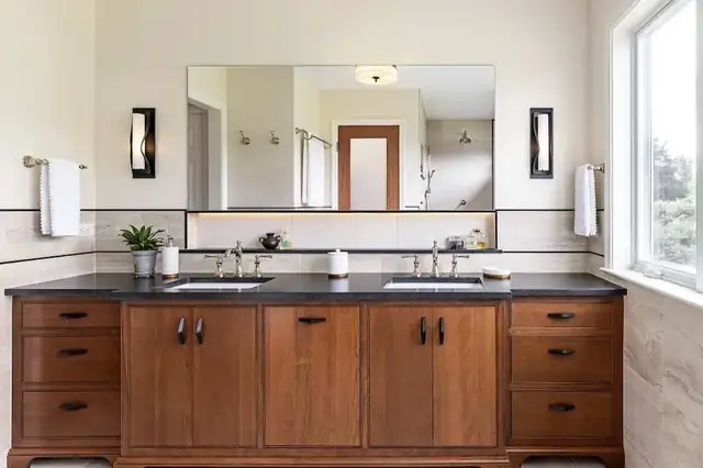 Bathroom with cherry double vanity, black countertop, wide frameless mirror and black wall sconces