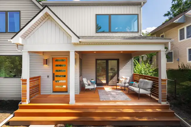 Home addition in Ann Arbor with a covered wood porch, board-and-batten siding and an orange front door