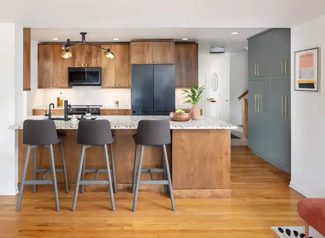 Kitchen with stained wood cabinets, a speckled granite island, gray counter stools and green pantry cabinets