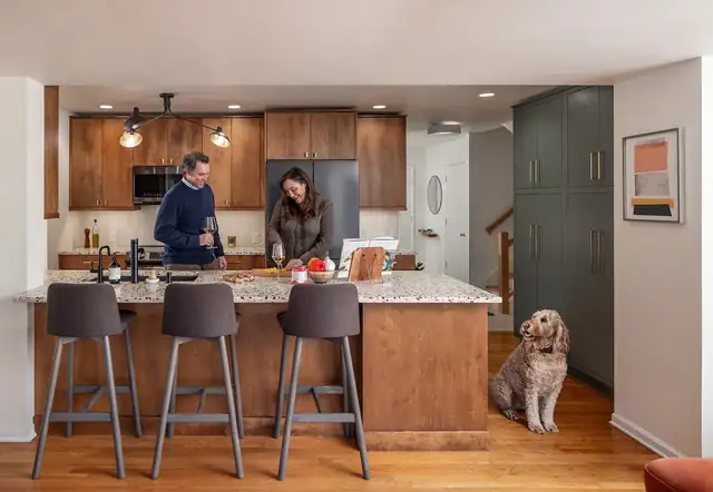 Open kitchen with wood cabinets, green pantry wall and a stone-top island with stools, with the family dog nearby